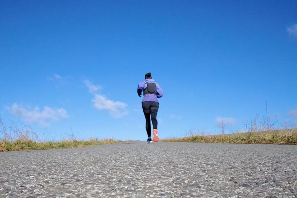 Trailrunnerin von hinten beim Laufen auf Asphalt, zentral im Bild